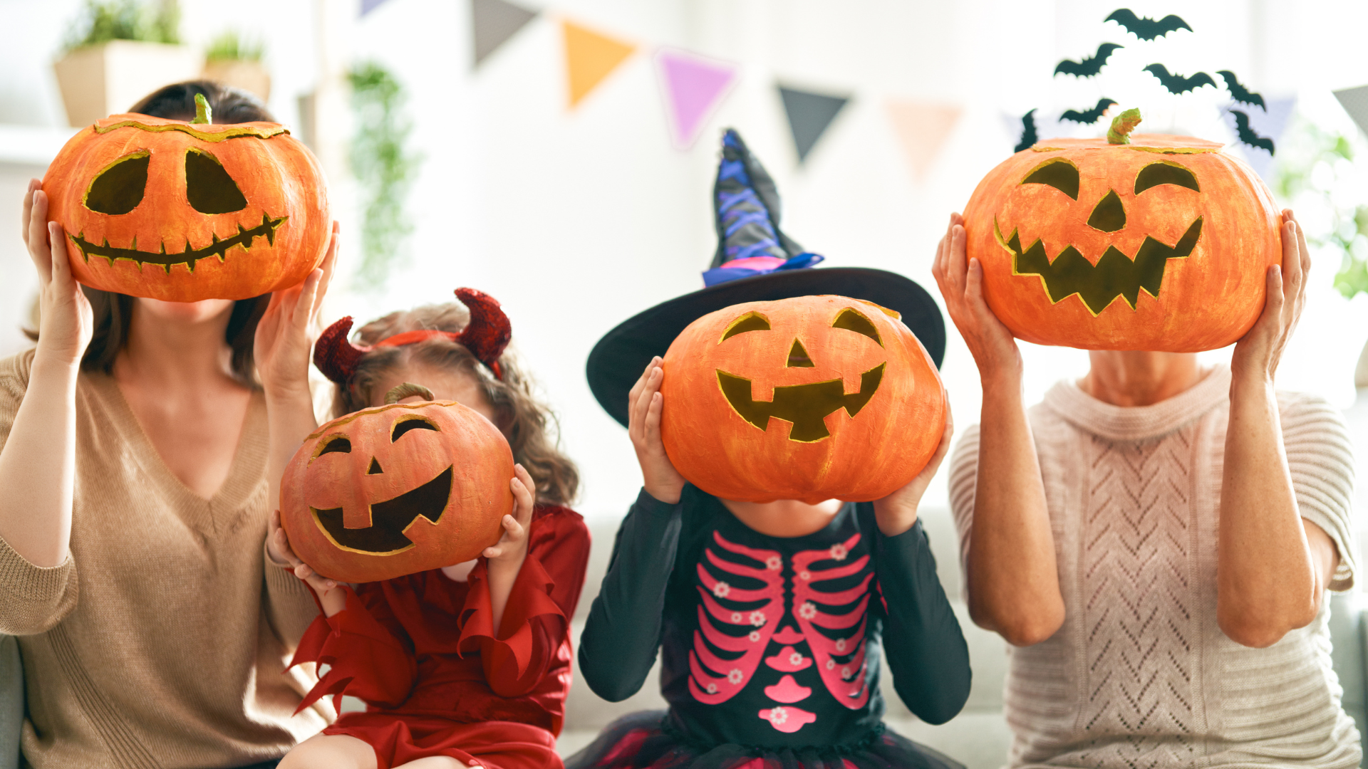 A family holds their fun, carved pumpkins over their faces with Halloween decorations around them. 