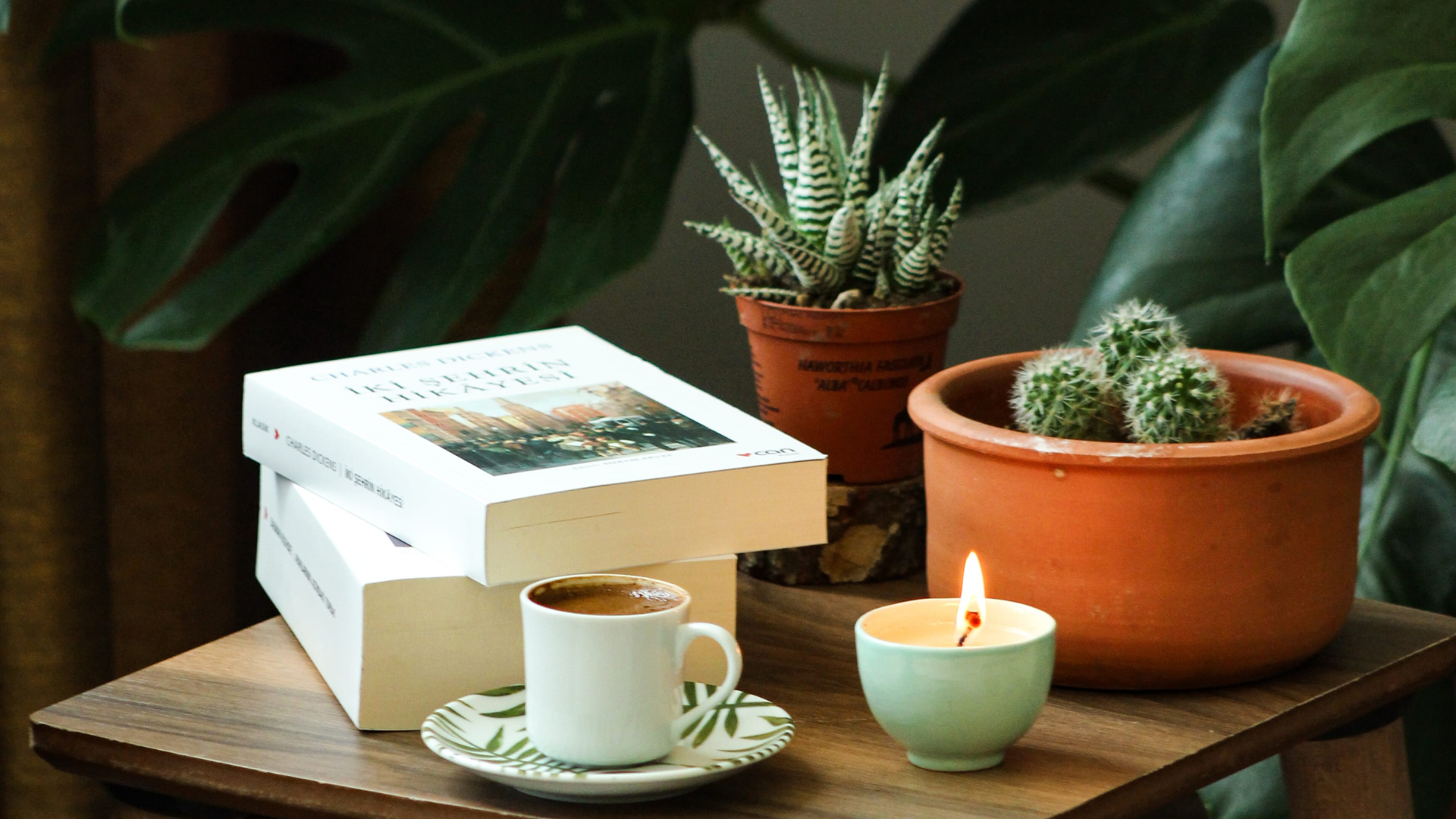 Some books, tea, plants, and a candle sit on a table, ready for a night honoring hygge. 