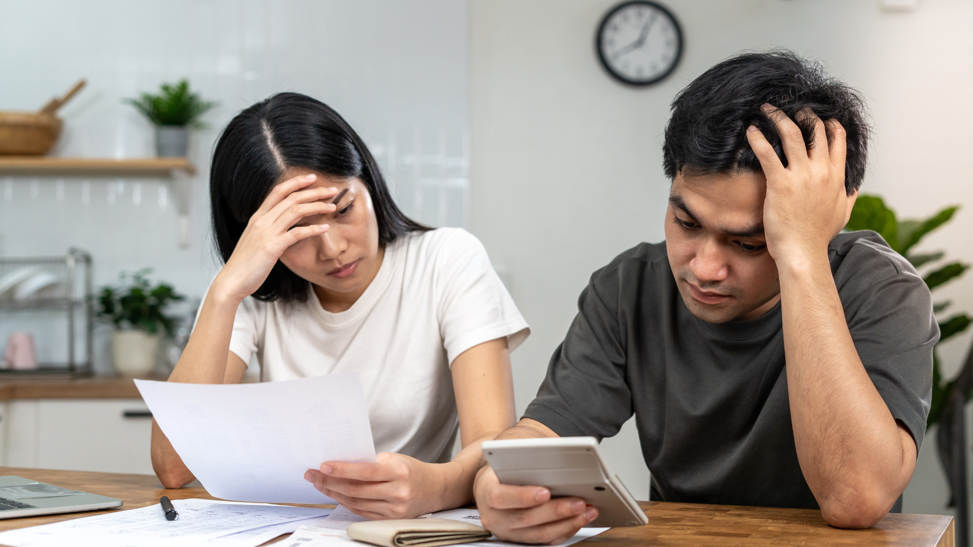 Untitled design (42) A couple sits in their kitchen, stressed as they struggle to manage their finances.