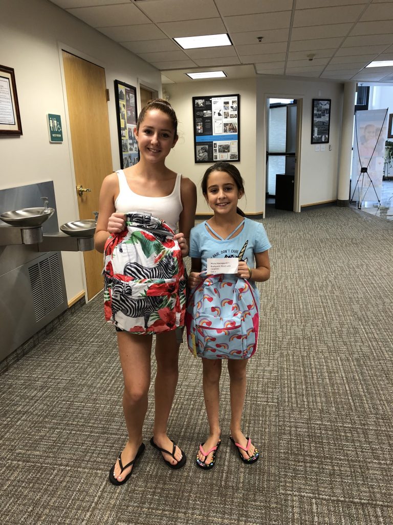 Two girls smiling holding backpacks