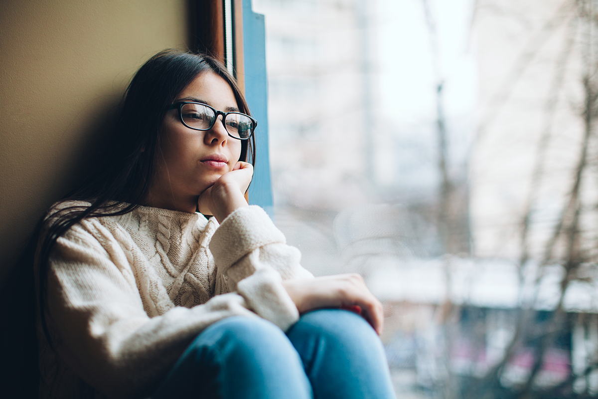 LGBTQIA+ teen sitting in front of window looking sad