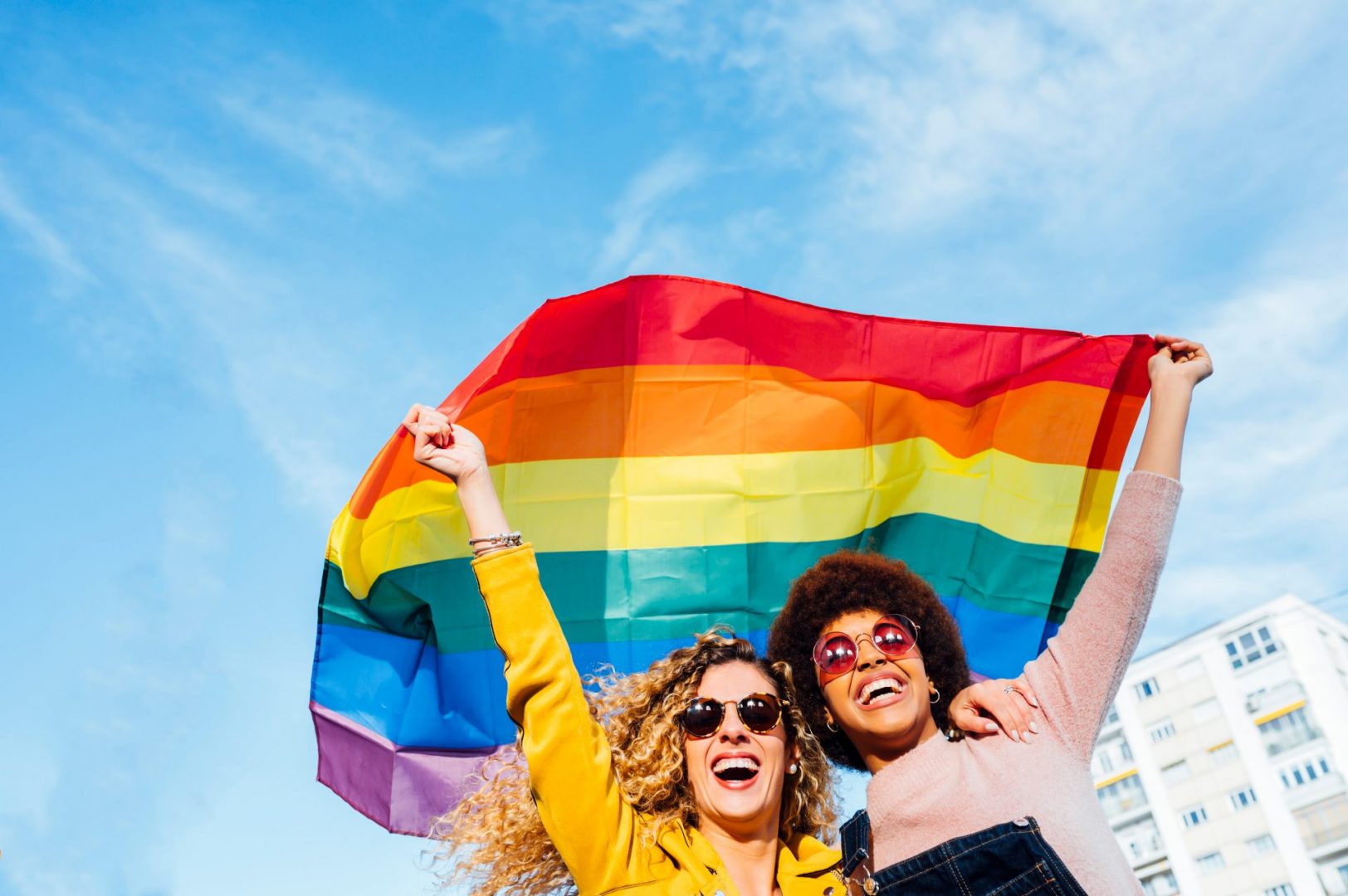 two women celebrating pride month and waving LGBTQIA+ pride flag