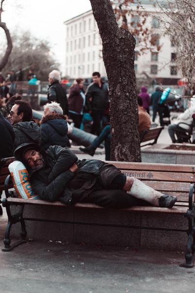 homeless man sleeping on bench in crowded park