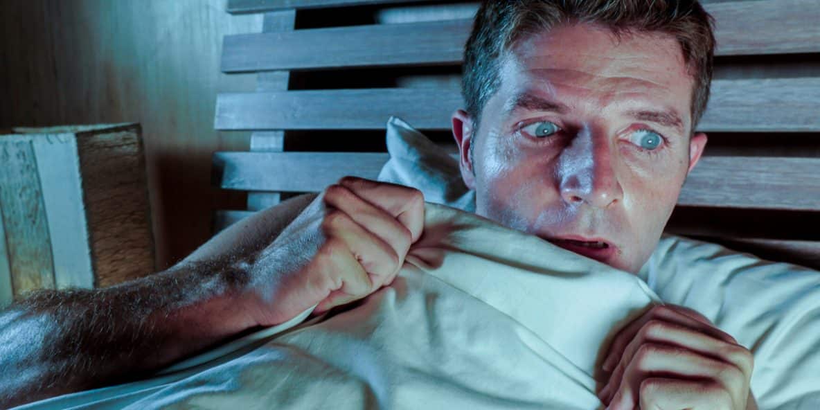 Paranoid man sitting in bed looking nervous