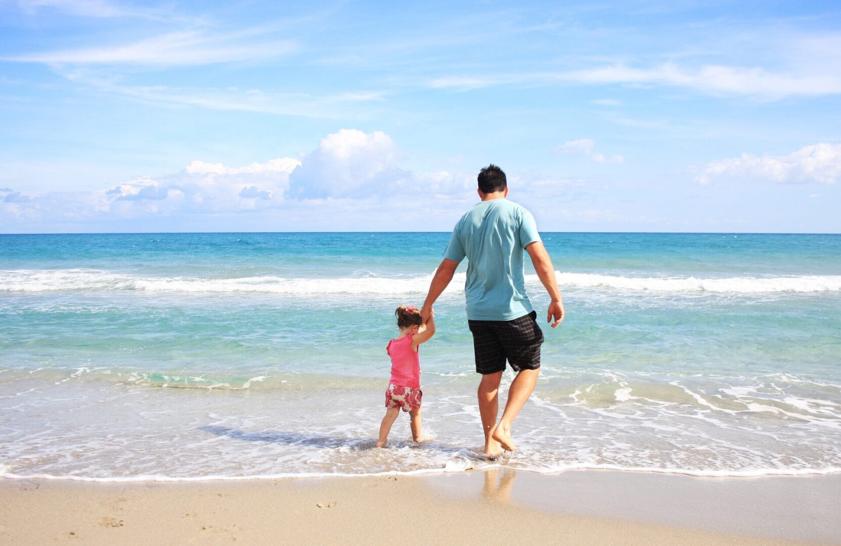 dad and daughter walking on the beach in the waves