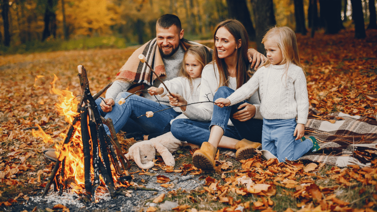Family sits around a bonfire roasting marshmallows.