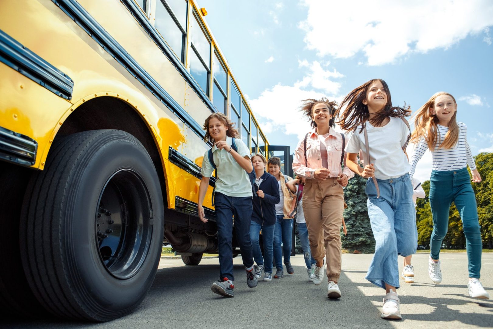 Group,Of,Children,Classmates,Running,From,School,Bus,Going,Back A group of smiling children at school wearing backpacks