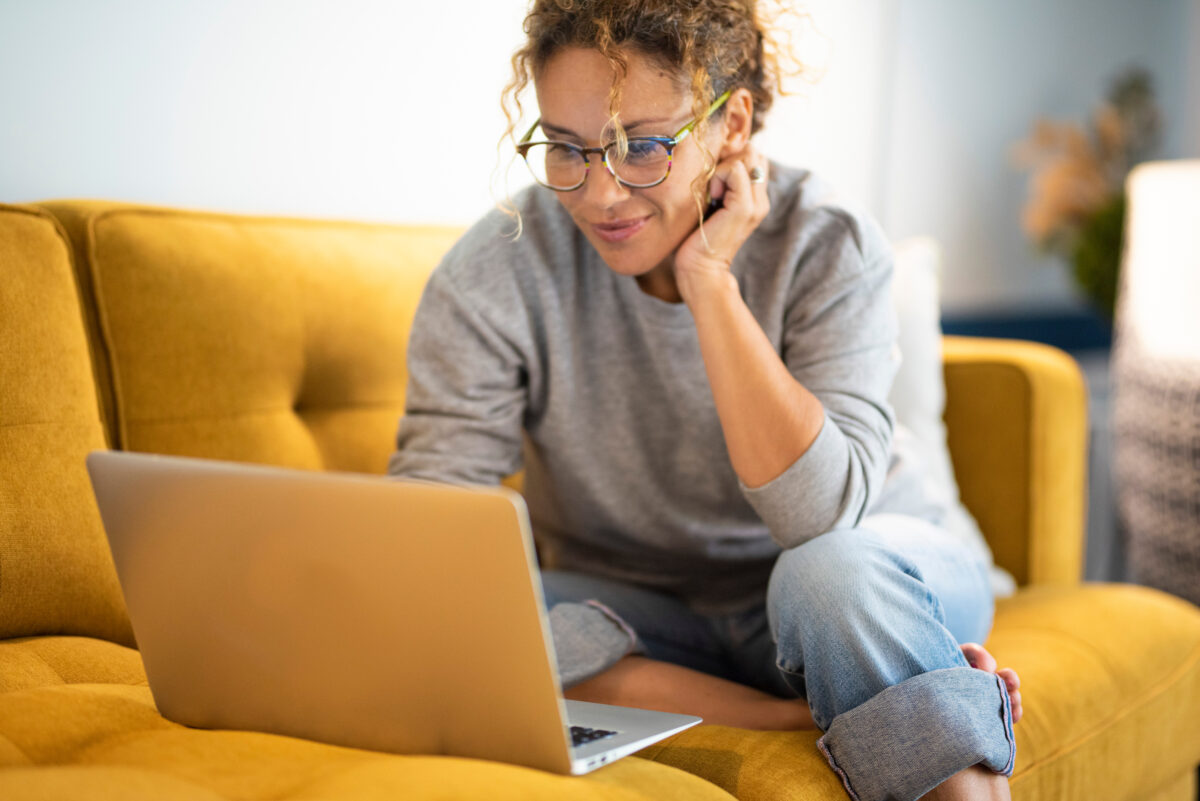Woman sitting on a couch smiling as she searches for healthcare options.
