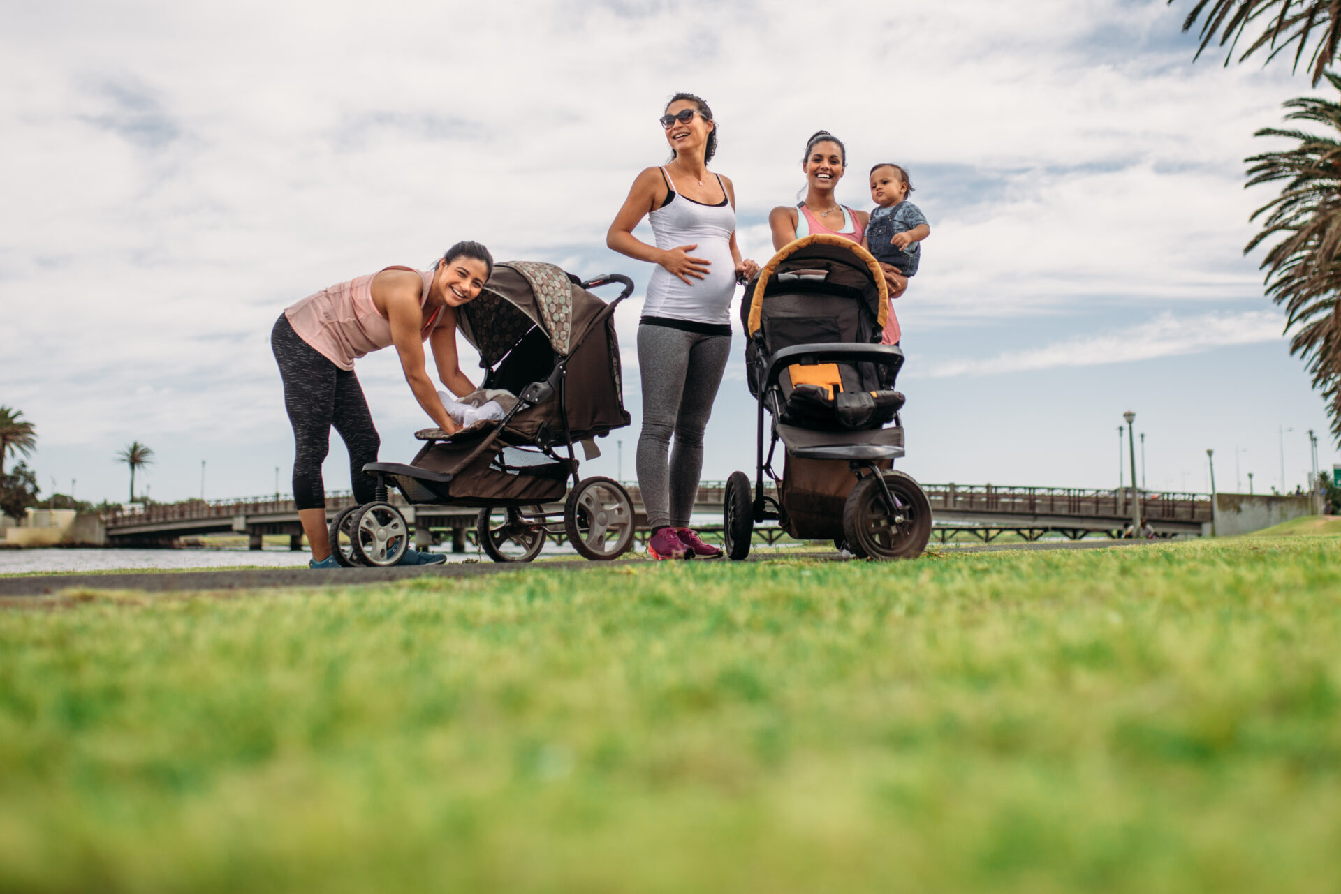 Young mothers standing in a park with their babies in strollers. Active moms relaxing after morning walk in park with their kids.