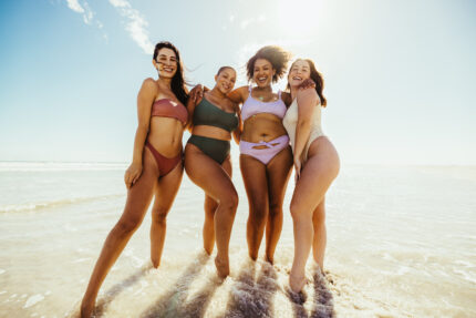 Group of cheerful young women embracing each other while wearing swimwear at the beach.