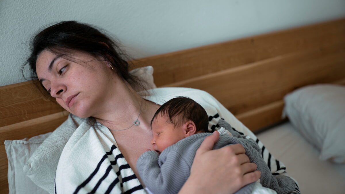 Tired mom lying down with newborn baby on her chest.