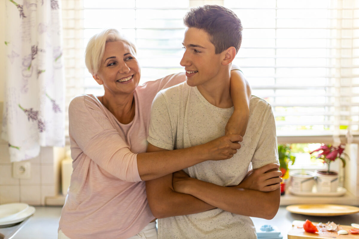 Mom hugging her teenaged son in their kitchen.
